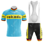 The Boule dOr Sunair Retro Short Sleeve Cycling Set features a blue jersey with yellow bands and rokado text in black. The matching bib shorts are black with yellow accents and the same text. Red and black stripes complete this vintage-inspired look.