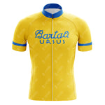 The Bartali Ursus Retro Cycling Jersey is yellow with short sleeves, featuring blue accents on the sleeves and collar. It showcases a retro cycling vibe with Bartali Ursus printed in blue across the chest and includes a full front zipper, reminiscent of Gino Bartalis era.