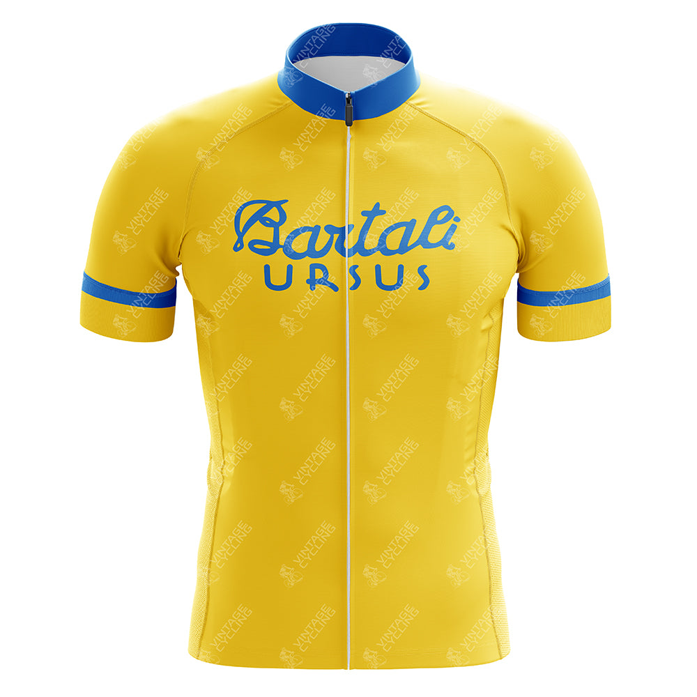 The Bartali Ursus Retro Cycling Jersey is yellow with short sleeves, featuring blue accents on the sleeves and collar. It showcases a retro cycling vibe with Bartali Ursus printed in blue across the chest and includes a full front zipper, reminiscent of Gino Bartalis era.