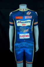 A mannequin displays the Mercatone Uno Wega Retro Cycling Jersey Set, vibrant blue with colorful sponsor logos like Mercatone Uno and Girmi, against a dark backdrop.