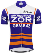 The Encendedor Zor Gemeaz Retro Cycling Jersey features white and blue panels, a design inspired by a vintage Spanish cycling team. ENCENDEDOR, ZOR, and GEMEAZ appear in bold white letters on the front with orange horizontal stripes at the bottom and branded logos on the chest and sleeves.