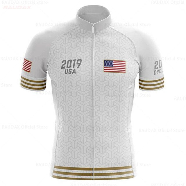 The USA White Gold Cycling Team Jersey features a geometric design with 2019 USA and the U.S. flag on the front, adorned with U.S. flags and gold stripes on both sleeves. Made from lightweight polyester, it offers comfort with its predominantly white and subtly patterned appearance.