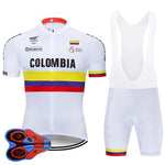 The Colombian Cycling Federation Retro Cycling Jersey Set features a white jersey with Colombia elegantly scripted on the chest. Vibrant red, yellow, and blue stripes adorn it. The matching white bib shorts mirror these stripes and include branded padding for added comfort.