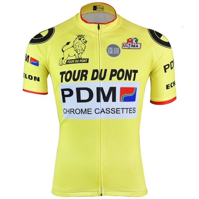 The Équipe Cycliste PDM Tour Du Pont Retro Cycling Jersey is yellow with black, white, and red sponsor logos, including Tour Du Pont, PDM, and Chrome Cassettes. It features a lion graphic and short sleeves with red trim for a vintage feel.