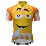 The M&Ms Yellow Cycling Jersey features a large, smiling yellow cartoon face with playful eyes and a white glove touching its chin. It has an orange polka-dot pattern at the top on a bright orange background and is crafted from lightweight polyester for optimal comfort.
