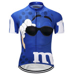 The M&Ms Blue Cycling Jersey features a large cartoon character with sunglasses, a white bow, and blue polka dots. A prominent m appears on the front. Made from lightweight polyester, it includes a center zipper and silicone waist strip for secure comfort.