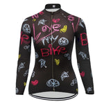 The Womens Long Sleeve Love My Bike Cycling Jersey features vibrant designs with phrases like Love my Bike, bike wheels, and hearts in pink, yellow, and blue on black. It includes a full front zipper for style and function.