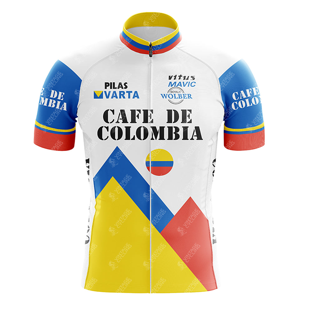 The Cafe D Colombia Retro Short Sleeve Cycling Set features geometric mountain designs in blue, yellow, and red— reminiscent of the Colombian flag. Cafe de Colombia text is adorned with logos for Pilas Varta, Vitus, Mavic, and Wolber above it.