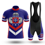 The Chief Short Sleeve Cycling Set features a blue, red, and white retro jersey with AA insignia, parachute logo, U.S. flag on the sleeve, and matching bib shorts with chevron design and emblem on the left leg.