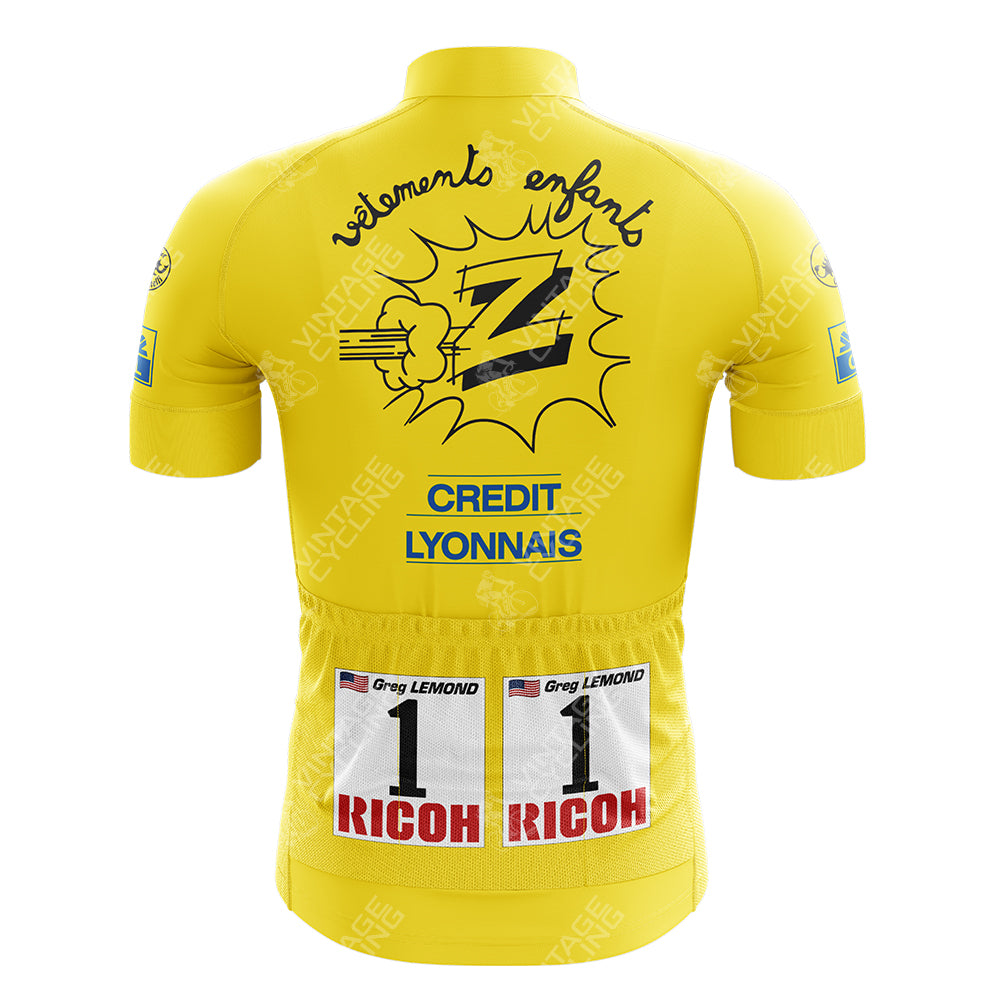The Credlt Lyonnals Retro Short Sleeve Cycling Set features a retro yellow jersey with a comic-style graphic, text vêtements enfant, Credit Lyonnais, a large Z and fist design. It includes two cycling bib numbers labeled “1” and sponsor logos.