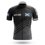 The Drinking Men Short Sleeve Cycling Set includes a black jersey with SCOTLAND and Scottish flags on the chest and sleeves, subtle diagonal stripes, a full zipper, and matching men's bib shorts for a complete cycling look.