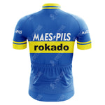 The Maes-Pils Rokado Retro Cycling Jersey, made from lightweight polyester, features a blue and yellow design with Maes Pils and Rokado on the back. It has a yellow stripe across the middle and short sleeves for optimal performance.