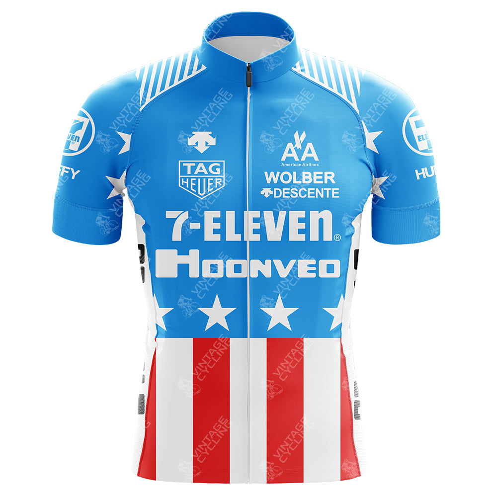 The 7-Eleven Hoonved USA Retro Cycling Jersey features a blue design with white stars on the chest and sleeves, red and white vertical stripes on the lower half, crafted from lightweight polyester with logos of 7-Eleven, Descente, etc.—ideal for Eddy Merckx bike fans craving a retro vibe.