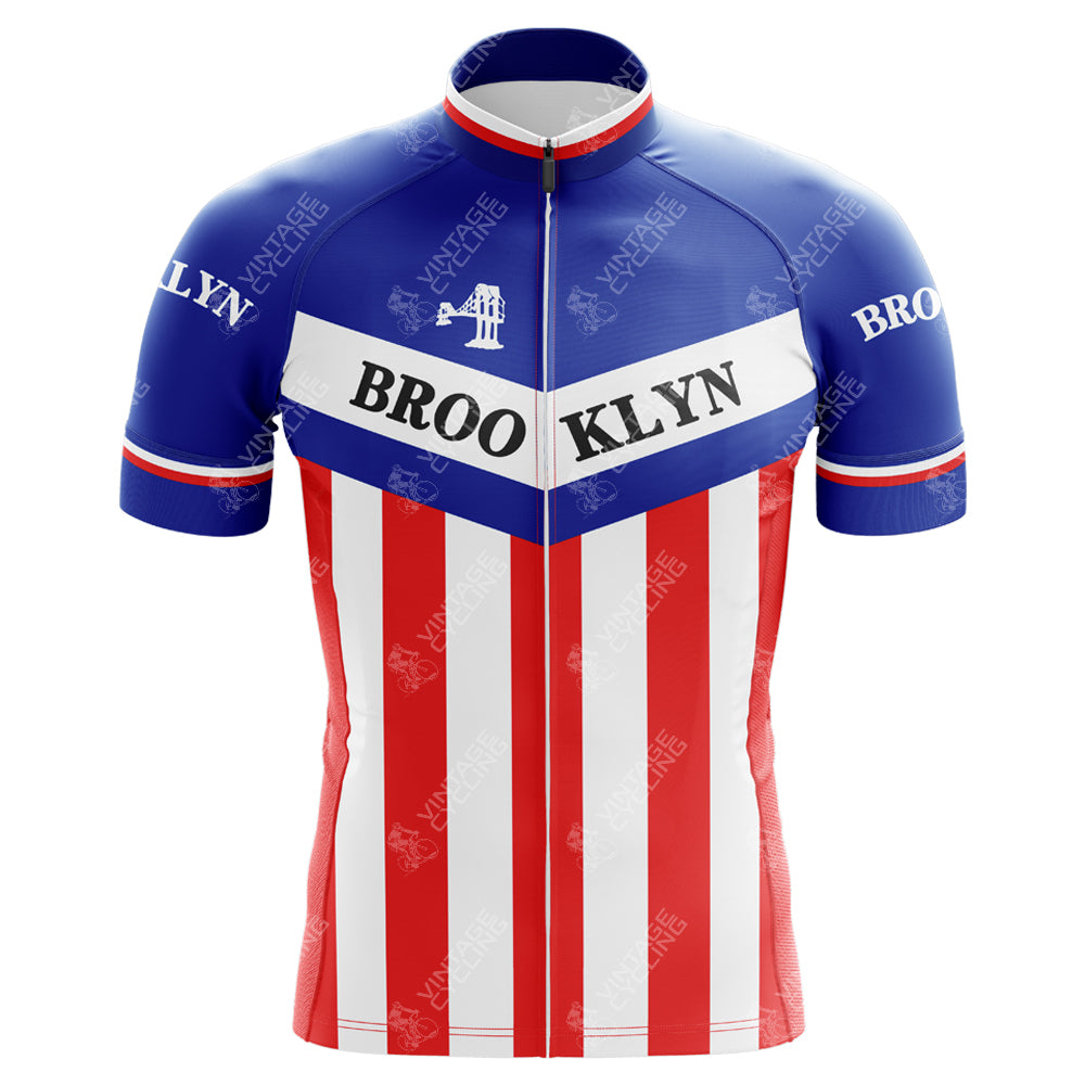 The Brooklyn Chewing Gum Retro Cycling Jersey features an iconic blue top with BROO KLYN across the chest, white midsection, and red stripe at the bottom. Inspired by Roger de Vlaeminck, it has a small bridge graphic near the BROOKLYN-adorned sleeves, echoing Brooklyns classic style.