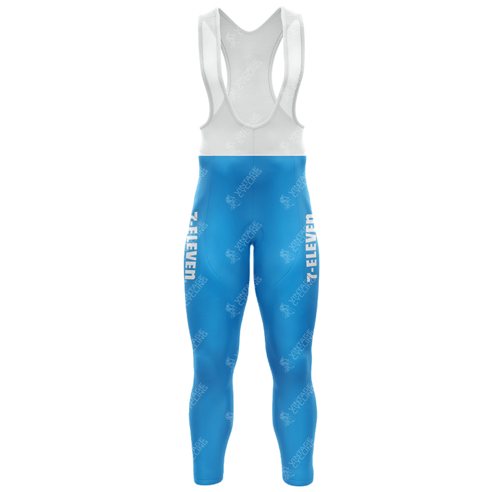 Blue cycling bib tights with white straps display 7-ELEVEN in white on the sides, part of the 1990s 7-ELEVEN Retro Long Sleeve Cycling Set. The fabric features a subtle pattern and branding, seamlessly blending functionality with a sleek look.