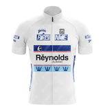 The Reynolds Aluminio Retro Cycling Jersey is white with short sleeves, blue and black logos like París Nice and Reynolds Aluminio, and features blue crown symbols along the bottom, capturing Pedro Delgados spirit.