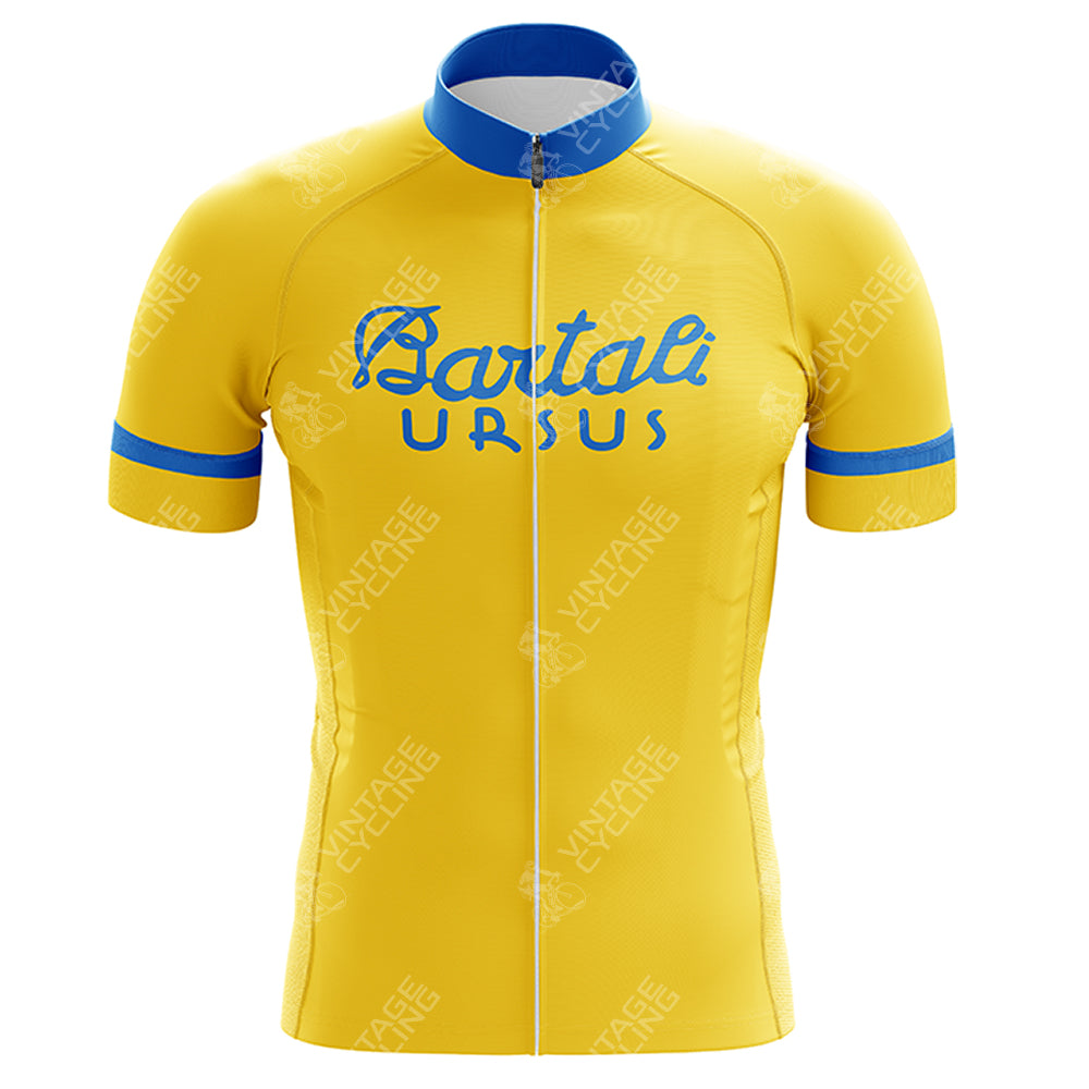 The VELDA Retro Short Sleeve Cycling Set is a yellow jersey with blue accents on the collar and cuffs, featuring Bartali-Ursus in blue script on the front and a central white zipper. The fabric includes subtle Vintage Cycling watermarks for a complete retro look.
