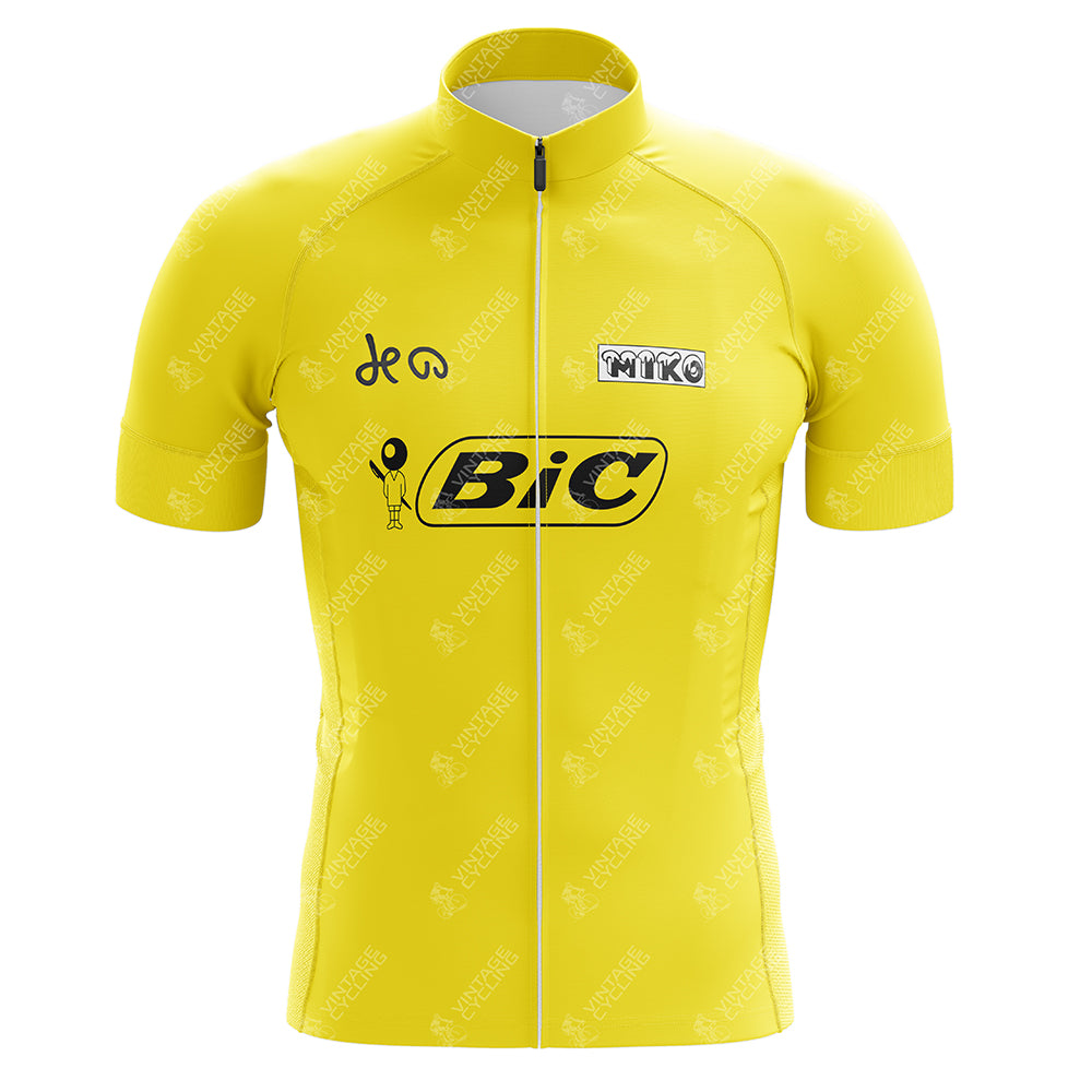 The BIC 1973 Luis Ocana Retro Cycling Jersey features a yellow retro design with a front zipper, black BIC logo on the chest, textured fabric with Vittoria branding, short sleeves, and a low-cut collar, inspired by Luis Ocanas iconic 1973 Tour de France win.
