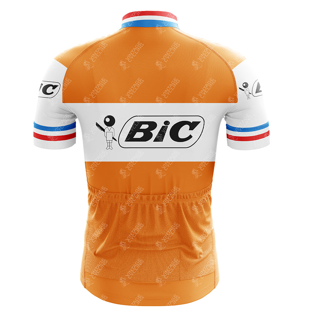 The BIC Orange-France Short Sleeve Retro Cycling Jersey, inspired by the iconic BIC Cycling Team, features an orange base with a white band displaying the Bic logo. The sleeves are adorned with red, white, and blue stripes near the cuffs, echoing Jacques Anquetils classic style.