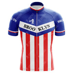 The Brooklyn Chewing Gum Retro Cycling Jersey features an iconic blue top with BROO KLYN across the chest, white midsection, and red stripe at the bottom. Inspired by Roger de Vlaeminck, it has a small bridge graphic near the BROOKLYN-adorned sleeves, echoing Brooklyns classic style.