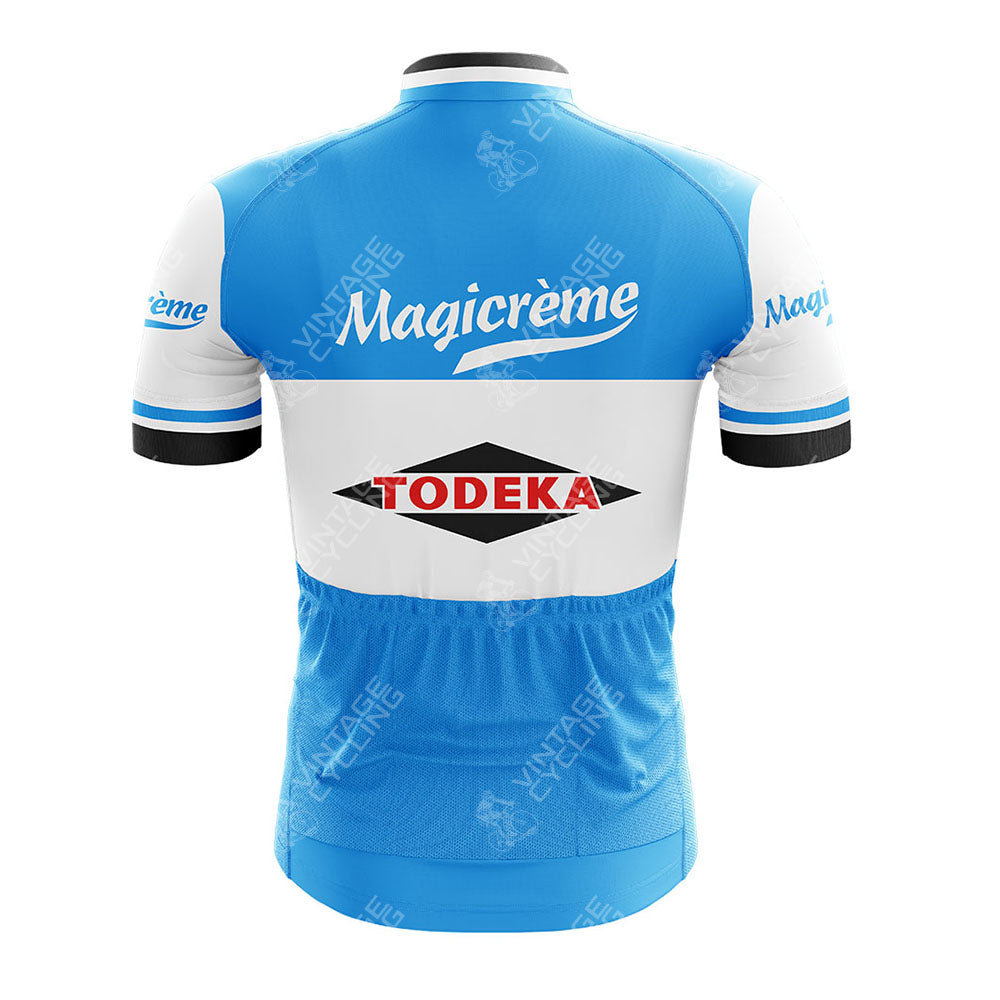 A blue and white Margnat Paloma Retro Short Sleeve Cycling Jersey, shown from the back, displays Magicrème in white across the upper back and a Todeka Magicreme logo with a black diamond center. Perfect for any retro cycling set.