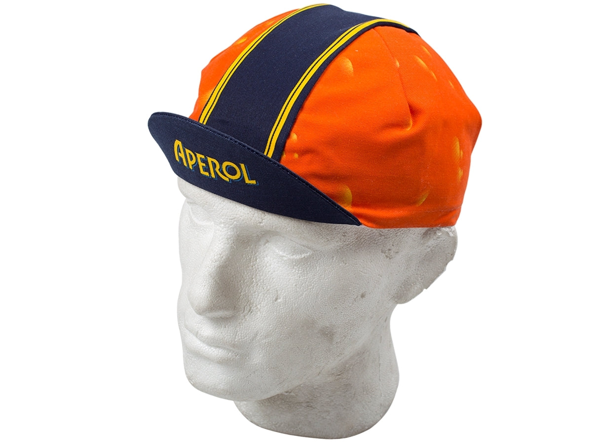 An Aperol Retro Cycling Cap, in bold orange and blue, adorns a white mannequin head. This classic design showcases APEROL on the brim with a blue stripe running from front to back, capturing vintage cycling style.