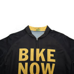 Close-up of the Bike Now Beer Later Cycling Jersey Set in black featuring BIKE NOW in bold yellow letters. The top zipper and size L label are partly visible, and it includes a gel seat pad for added comfort during long rides.
