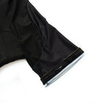 Close-up of a Bike Now Beer Later Cycling Jersey laid flat, focusing on the black, short-sleeved fabric. The smooth, slightly glossy material features a stitch near the edge, with lighting enhancing its texture and structure.