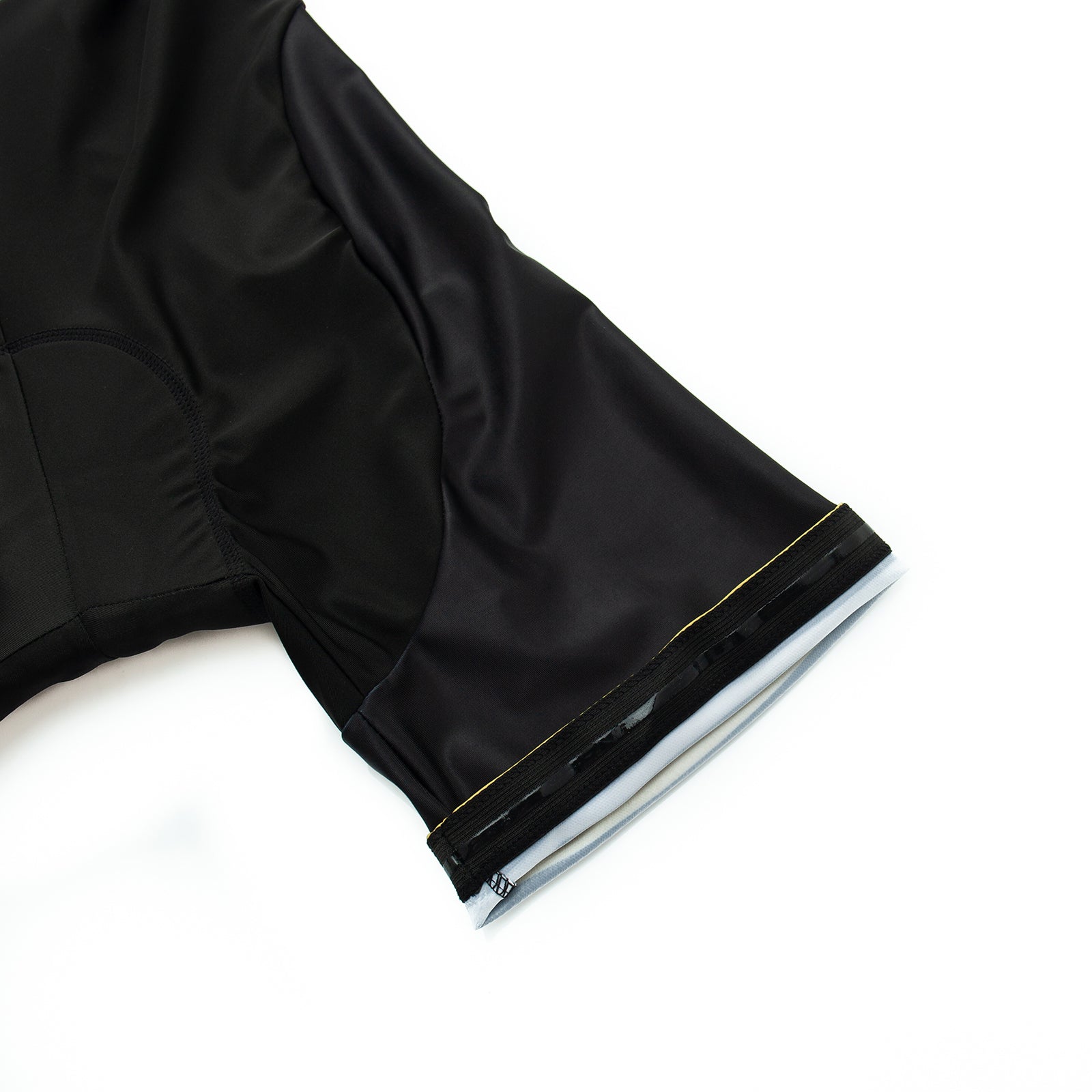 Close-up of a Bike Now Beer Later Cycling Jersey laid flat, focusing on the black, short-sleeved fabric. The smooth, slightly glossy material features a stitch near the edge, with lighting enhancing its texture and structure.