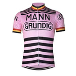 The Mann Grundig Belgium Retro Cycling Jersey is a lightweight polyester pink jersey with black stripes, featuring MANN and GRUNDIG in bold black letters on the front and sleeves. The cuffs are adorned with red, yellow, and black bands for a classic look.