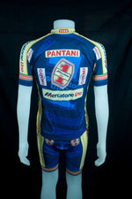 A vibrant retro cycling jersey shown from the back features blue, yellow, and red colors. With Pantani and sponsor logos Girmi and Mercatone Uno, this Mercatone Uno Wega Retro Cycling Jersey Set honors Marco Pantanis legendary rides.
