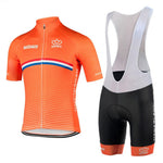 The Netherlands Cycling Team Retro Cycling Jersey Set includes an orange jersey with Nederland text, a zipper, and a white, blue, and red chest stripe. The black bib shorts feature white straps and an orange band at the leg ends, representing the classic team style.