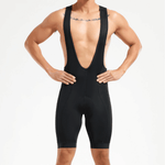 A person stands with hands on hips against a white background, showcasing the Pro Team Cycling Bib Shorts in black. Designed for performance and comfort, they feature wide straps over the shoulders, and a tattoo is visible on the upper chest.