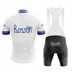 The Frigos Boston Retro Cycling Jersey Set includes a white and blue jersey with the Frigos Boston logo, featuring a blue collar and cuffs for comfort. It comes with matching black bib shorts displaying the same logo on the side.