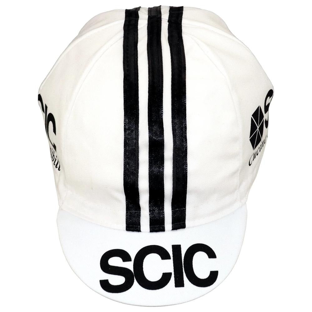 This retro cycling cap, named SCIC Cucine Conponibili, showcases three vertical black stripes and bold logos on the front and sides. Add classic style to your ride by purchasing it at vintagecycling.shop.