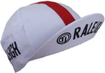 The TI Raleigh Retro Cycling Cap is a vintage-style white cap with a red stripe running front to back, showcasing RALEIGH in bold black print on the left side and brim, perfect for fans of iconic cycling style.