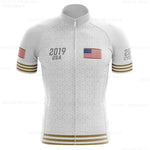 The USA White Gold Cycling Team Jersey features a geometric design with 2019 USA and the U.S. flag on the front, adorned with U.S. flags and gold stripes on both sleeves. Made from lightweight polyester, it offers comfort with its predominantly white and subtly patterned appearance.