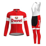 The Womens Duvel Beer Retro Cycling Jersey Long Set includes a red, white, and black long-sleeve jersey with winter fleece and a bib. It features a front zipper and Duvel in bold on both the jersey front and the side of the shorts, complete with a text logo and emblem.