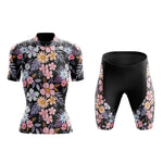 The Womens Floral Cycling Jersey Set is a lightweight polyester ensemble that features pink, white, and orange flowers with green and purple leaves on a black background. The short-sleeved jersey pairs perfectly with the shorts, which include gel seat pads for extra comfort.