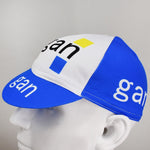 The Gan Retro Cycling Cap in blue and white displays gan in black and white on the side and brim, alongside classic retro elements with blue and yellow squares on the front. Displayed on a mannequin head, its available at vintagecycling.shop.