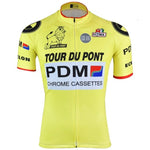 The Équipe Cycliste PDM Tour Du Pont Retro Cycling Jersey is yellow with black, white, and red sponsor logos, including Tour Du Pont, PDM, and Chrome Cassettes. It features a lion graphic and short sleeves with red trim for a vintage feel.