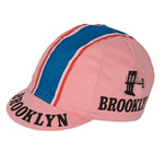 The Brooklyn Retro Cycling Caps showcase a classic pink design with blue and white stripes. BROOKLYN is boldly displayed on the brim and sides in black, alongside a black bridge silhouette for a nostalgic nod to Brooklyn Chewing Gum.