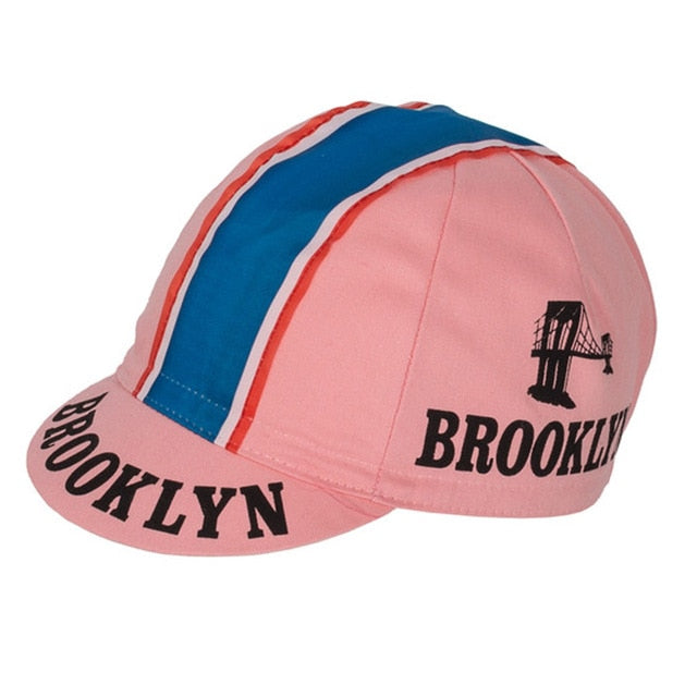 The Brooklyn Retro Cycling Caps showcase a classic pink design with blue and white stripes. BROOKLYN is boldly displayed on the brim and sides in black, alongside a black bridge silhouette for a nostalgic nod to Brooklyn Chewing Gum.