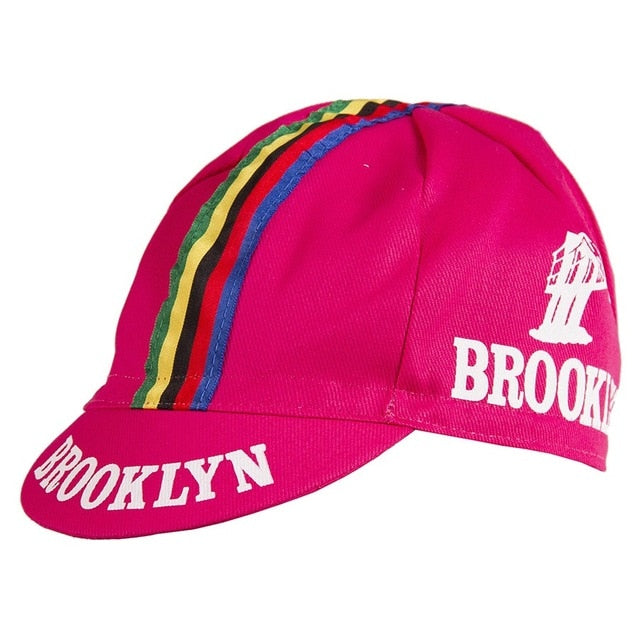 The Brooklyn Retro Cycling Cap is pink with BROOKLYN in white across the front and side, featuring a classic design adorned with vibrant stripes and a bridge logo, reminiscent of Brooklyn Chewing Gums iconic style.