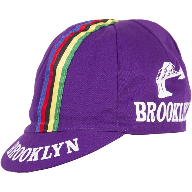 The Brooklyn Retro Cycling Cap boasts a classic purple design with a bold rainbow stripe from front to back. BROOKLYN is printed in white on the side and brim, reminiscent of Brooklyn Chewing Gum, and features a bridge graphic for added nostalgic appeal.