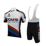 The Équipe Cycliste PDM (Chrome Cassettes) Retro Cycling Jersey Set includes a white short-sleeved jersey with black, red, blue, and green accents featuring PDM and Chrome Cassettes text, paired with black bib shorts that complement the vibrant design.
