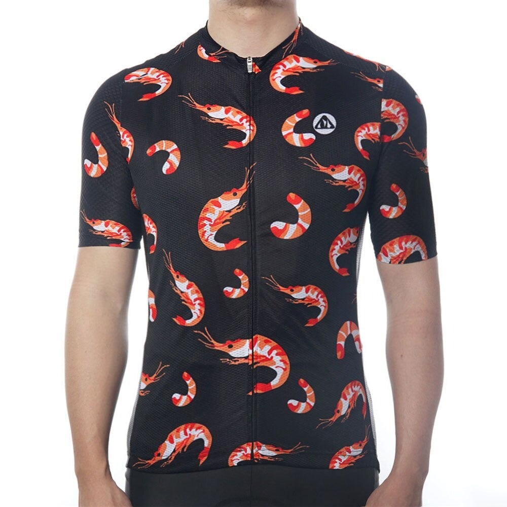 A person wearing the Shrimp Cycling Jersey, featuring a repeating pattern of orange and white shrimp designs. This performance jersey is made from lightweight polyester, has a full front zipper, and includes a small circular logo on the chest.