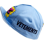 The Vetements Team Z Retro Cycling Cap is light blue with a colorful comic-style design, VETEMENTS printed on the side, and features vibrant yellow and pink graphic accents. Its short brim and fitted shape complete this classic accessory.
